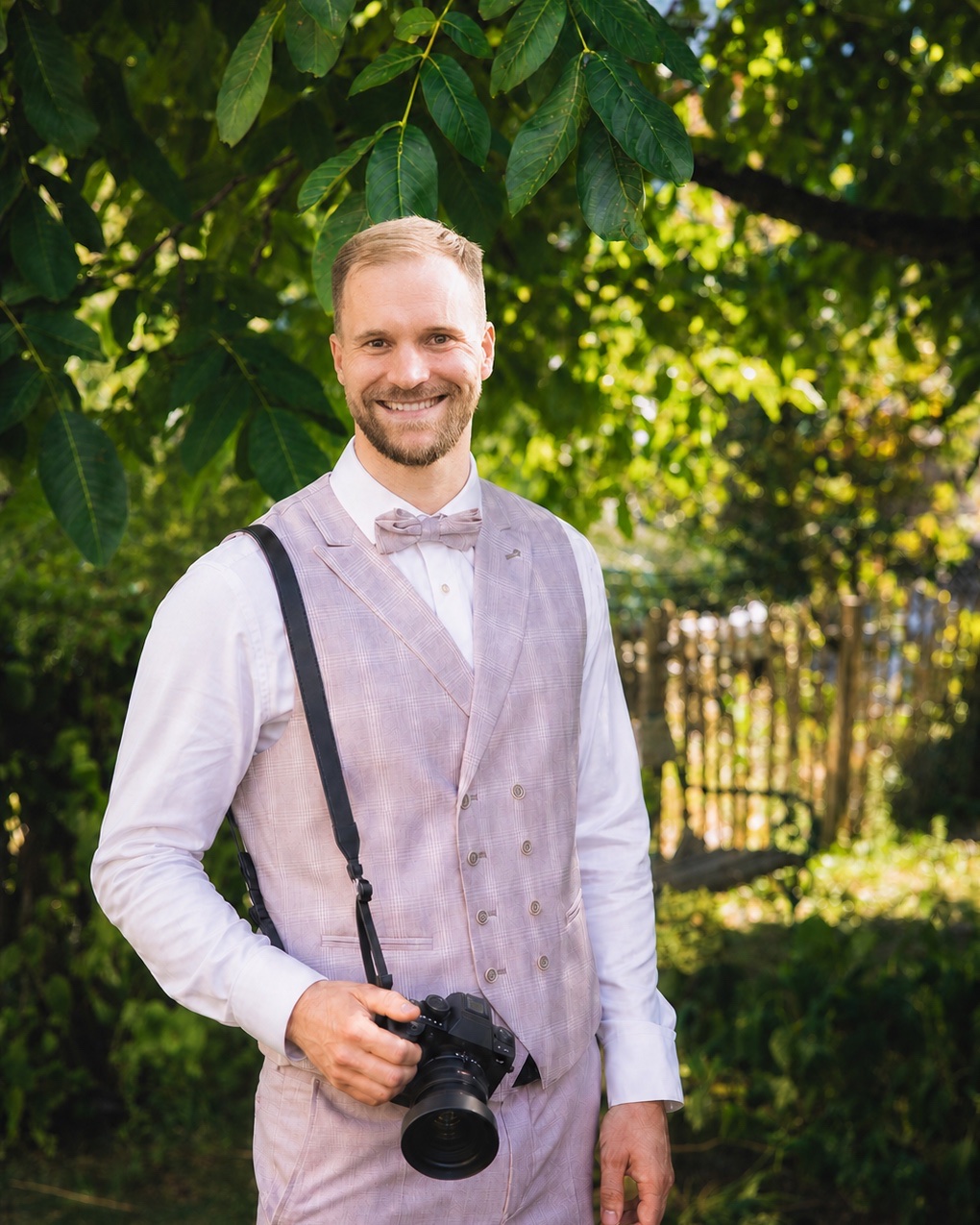 Fotograf Richard Kriss lächelt mit seiner Kamera im Grünen